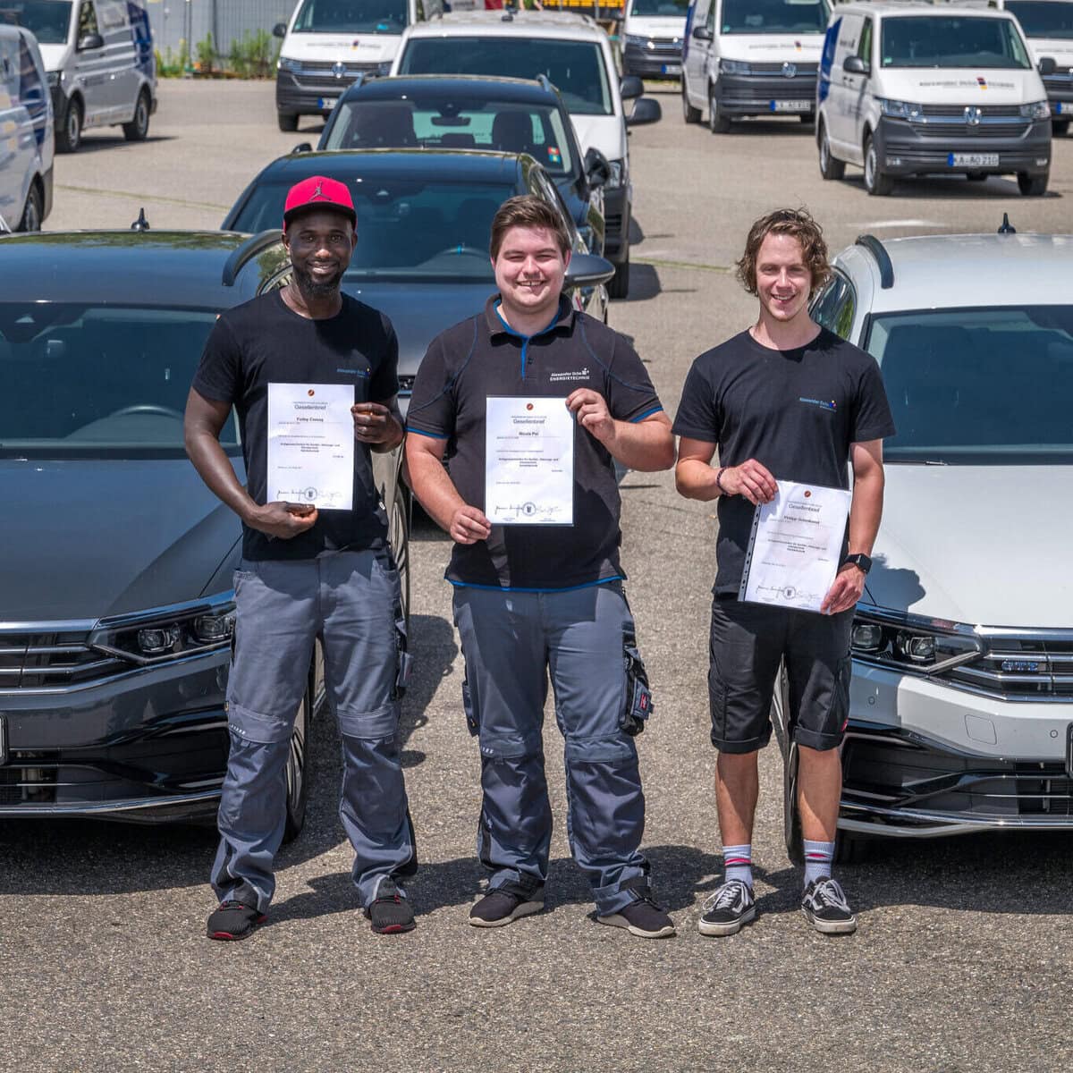 Drei junge Menschen mit Zertifikaten vor Autos in Bechem, Ghana.
