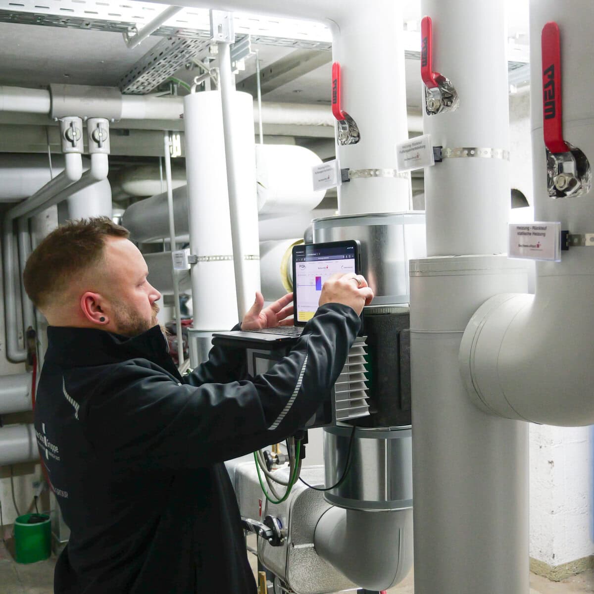 Techniker kontrolliert Heizungs- und Pumpensystem in Industrieanlage.